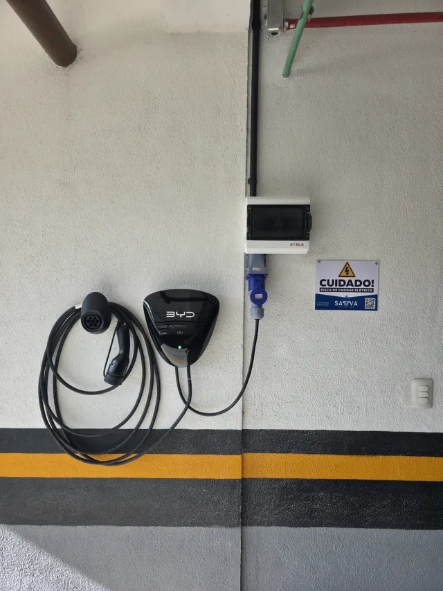 Carregador de carro elétrico instalado em garagem de condomínio, com sinalização de segurança