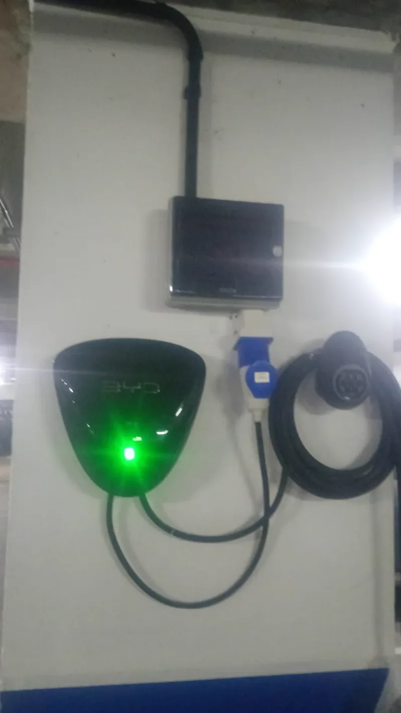 Carregador veicular instalado em parede branca, com luz refletida ao fundo