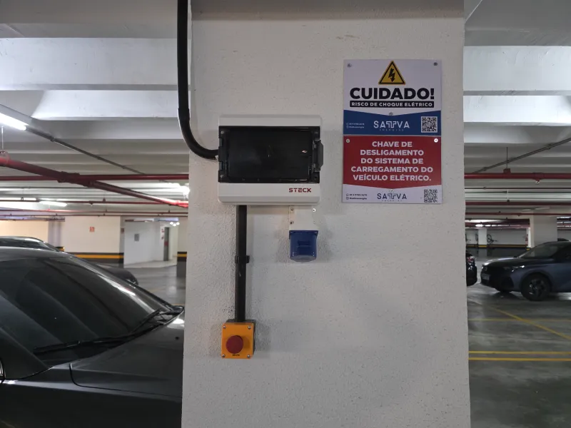 Quadro elétrico com chave de desligamento e botão de emergência, ao lado de veículo estacionado