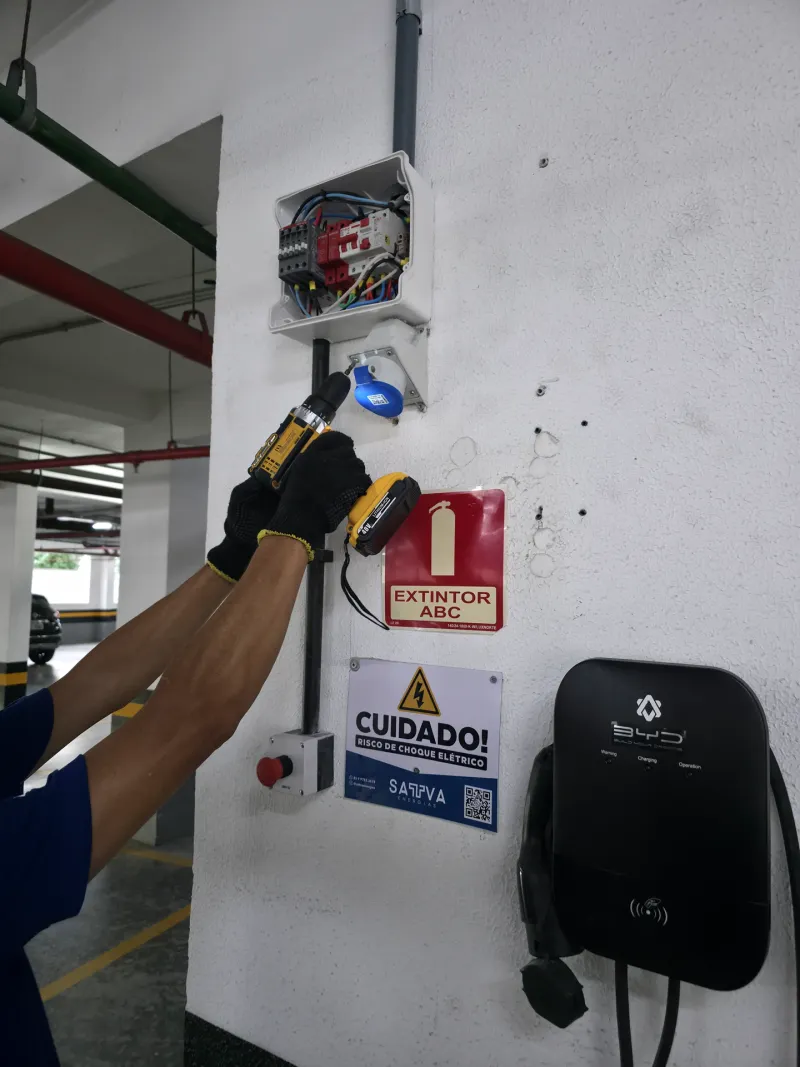 Técnico instalando tomada industrial, com carregador veicular ao lado